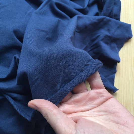 Hand holding a fabric, bamboo French Terry, in Indigo, to show the texture. Sew Not Complicated